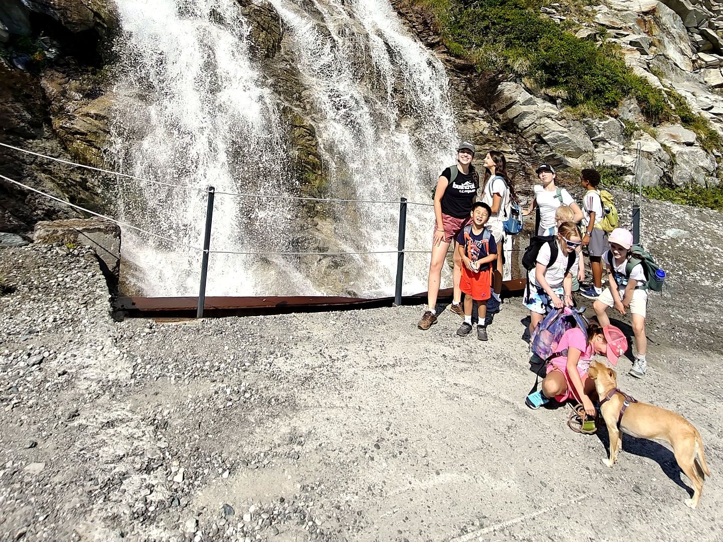 Group of campers and a dog in front of a waterfall on a mountain hike
