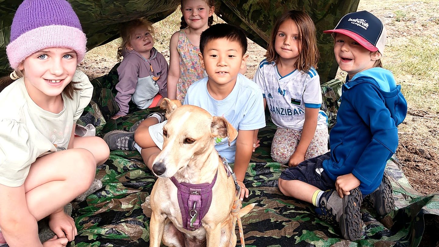 Young campers and a dog inside the shelter they built