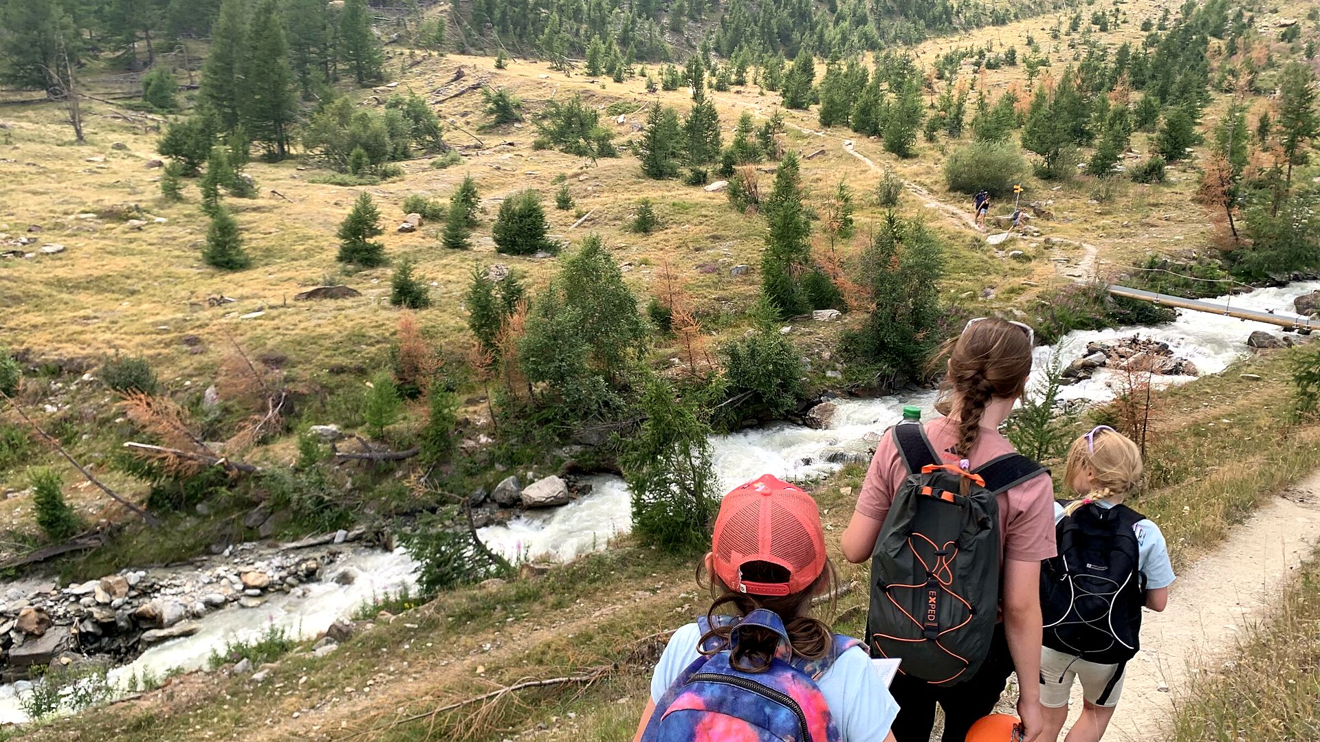 Peak Adventurers hiking through a river valley with backpacks near Saas-Fee