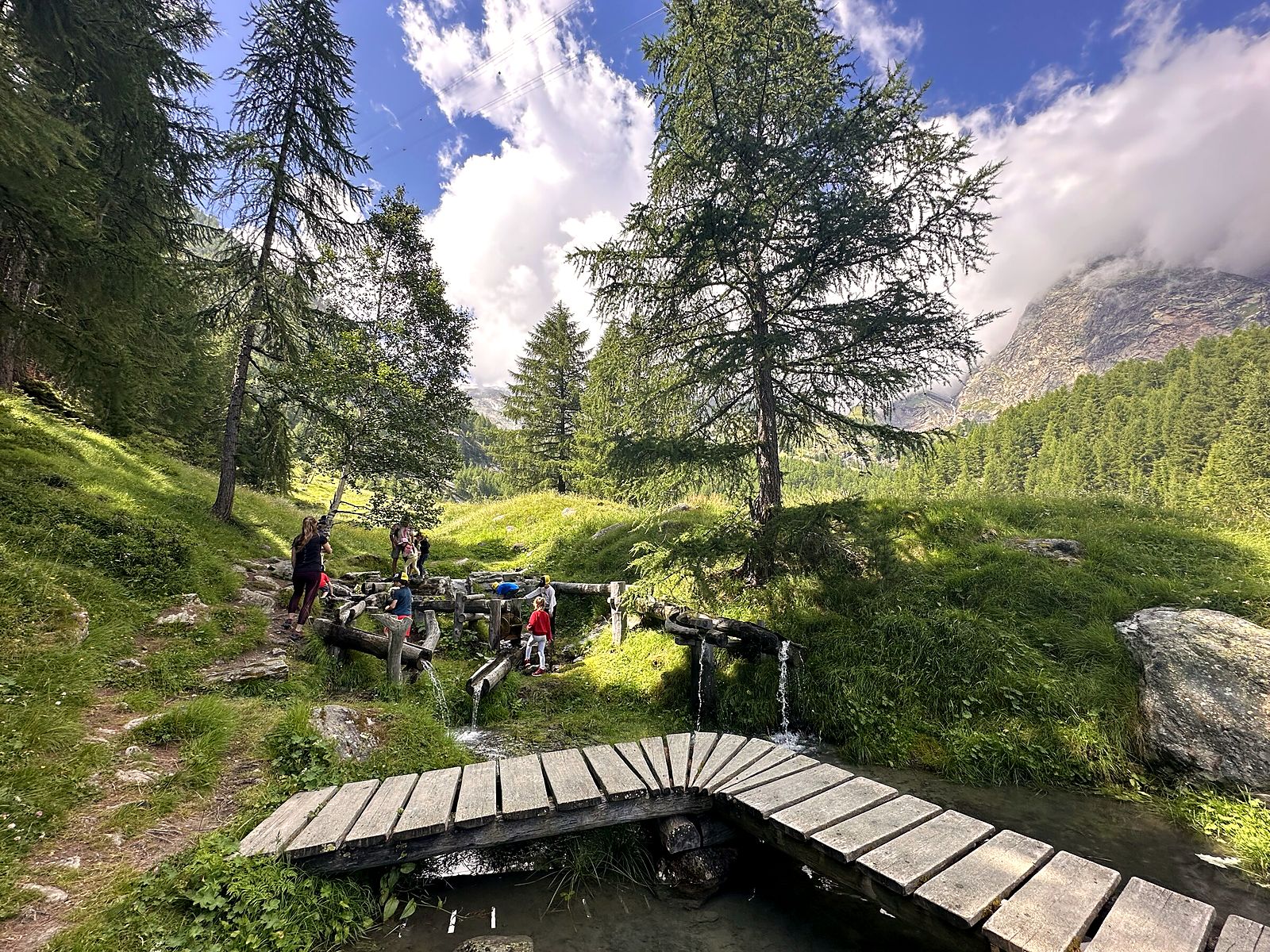 Little Explorers playing in the water from a wooden bridge near Saas-Fee